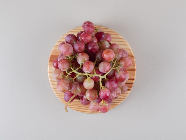 Red grape clusters on a wooden platter on marble background